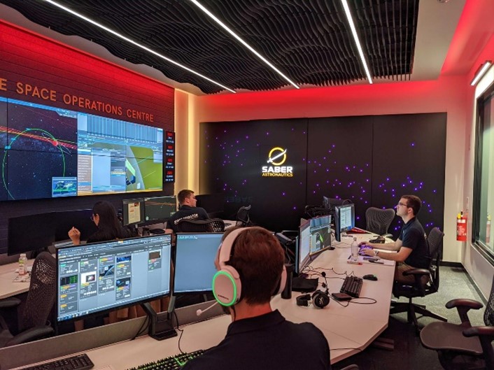 A group of people sitting around a table working at the Saber’s Responsive Space Operations Centre (RSOC)