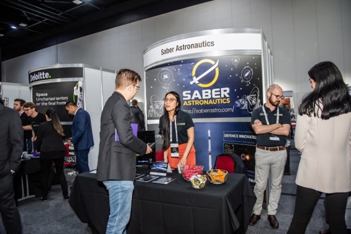 A group of people standing around a Saber stall at what appears to be an expo