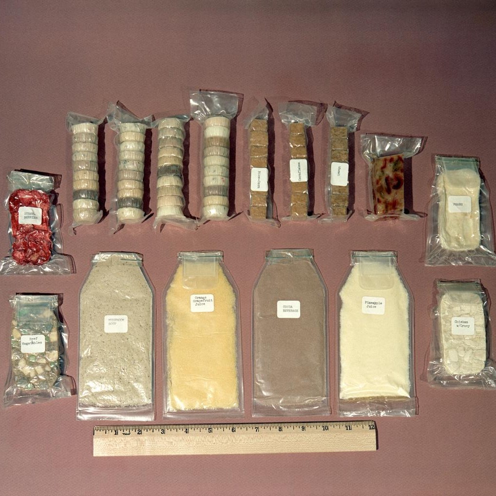 Food kit used by Mercury astronauts. Some is dehydrated and needs water, other packets are ready to eat. Size is measured relative to a ruler. Included are packets of mushroom soup, orange-grapefruit juice, cocoa beverage, pineapple juice, chicken with gravy, pears, strawberries, beef and vegetables and other assorted food containers. Photo credit: NASA