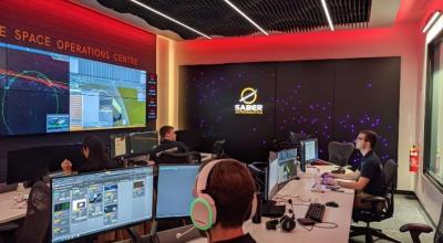 A group of people sitting around a table working at the Saber’s Responsive Space Operations Centre (RSOC)