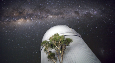 Astronomical observatory at night with view of galaxy behind.