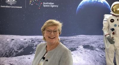 Portait of Head of Agency, Dr Megan Clark AC in front of a screen showing an astronaut on the moon facing with earth in the background.