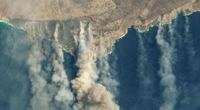 Australian coastline from above showing both tan coloured smoke and white clouds.