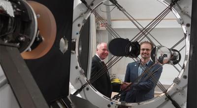 Australian Space Agency and EOS Space Systems leaders shake hands, reflected in the lens of space tracking equipment at the observatory.