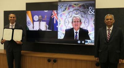 Two men standing in front of a television, with a third man on the screen. The man on the left holds the signed documents.