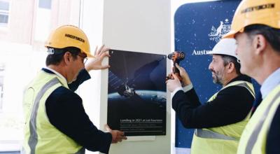 Three workers installing at a plaque of a satellite memorializing the opening of the centre