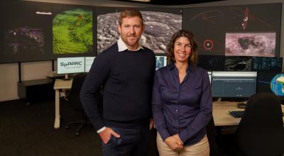 Two people standing in front of a computer, engaged in teamwork.
