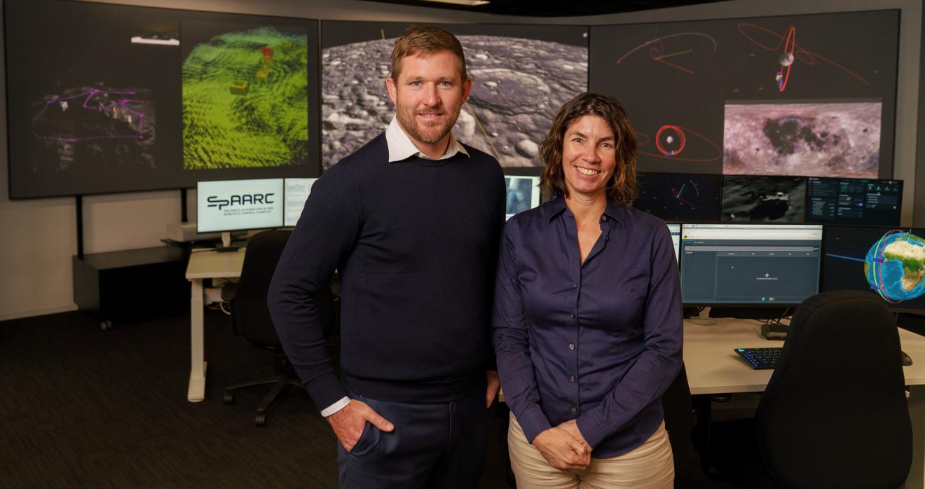 Two people standing in front of a computer, engaged in teamwork.