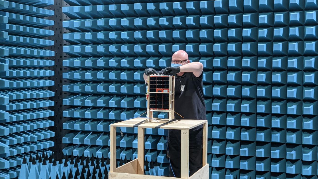 DSTG Engineer Darin Roberts attaches a radio frequency cable to the engineering model spacecraft during anechoic chamber testing at REDARC Defence & Space.