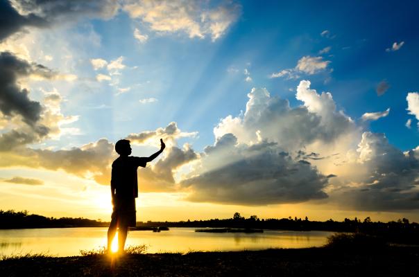 Silhouette of person taking selfie in-font of sunrise