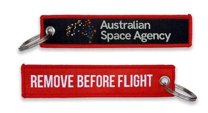 Triangle material key ring with Space Agency branding on one side and words 'Remove before flight' on the other