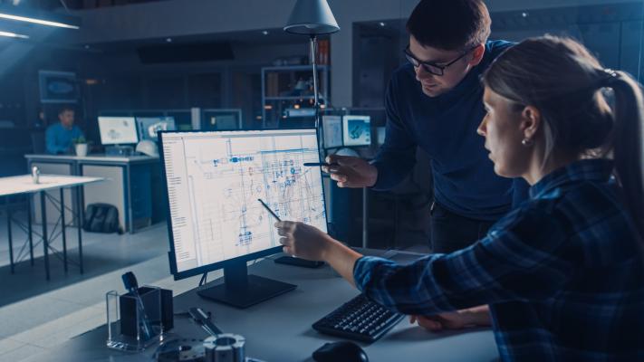 Two people standing in front of a computer, engaged in teamwork.