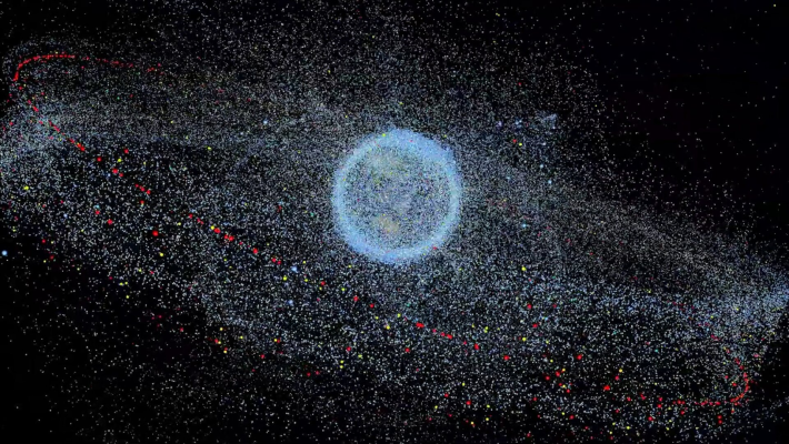 An image of the Earth appears on a black background. The Earth is swarmed by satellites and space debris that form a glowing, granular cloud around it.
