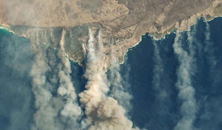Australian coastline from above showing both tan coloured smoke and white clouds.